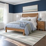 Diagonal angled room view showing the left side of a transitional sleigh bed with a low footboard, in a navy-walled bedroom.