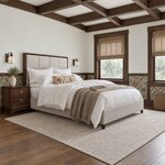 Diagonal angled room view showing the right side of a modern upholstered bed with tapered feet, in a beamed Craftsman room.
