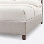 Footboard close-up of a modern upholstered bed, showing the squared upholstered corner and a short tapered leg.