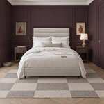 Front room view of a modern upholstered bed with a horizontally channeled headboard, in a plum-paneled bedroom.