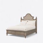 Diagonal angled view showing the left side of a farmhouse upholstered bed, with a scalloped headboard and nailhead trim.