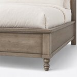 Footboard close-up of a farmhouse upholstered bed, showing the overhanging cap rail, a recessed panel and a turned foot.