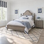Diagonal angled room view showing the left side of a farmhouse upholstered bed with turned feet, in a wainscoted bedroom.