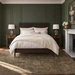 Front room view of a minimalist panel bed with a tall two-panel headboard, in a green-paneled bedroom with a fireplace.