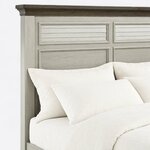 Headboard close-up of a coastal panel bed, showing shutter-style louvered panels over flat recessed panels and a crown cap.