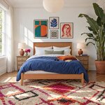 Front room view of a mid-century panel bed with a low footboard, in a bright eclectic bedroom with a gallery wall.