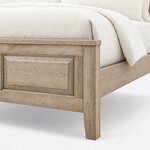 Footboard close-up of a traditional panel bed, showing the overhanging cap rail, a raised panel and a tapered square leg.