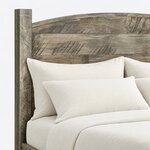 Headboard close-up of a rustic panel bed, showing horizontal planks under an arched top rail beside a square post.