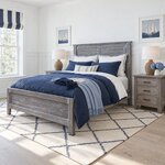 Diagonal angled room view showing the left side of a farmhouse panel bed with a louvered headboard, in a wainscoted bedroom.