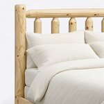 Headboard close-up of a rustic log bed, showing tapered-top log spindles under a round top rail beside a round post.