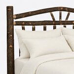 Headboard close-up of a rustic log bed, showing the arched log crest, sunburst spokes and round spindles beside a log post.