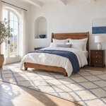 Diagonal angled room view showing the left side of a contemporary sleigh bed with curved posts, in a white plaster bedroom.