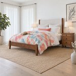 Diagonal angled room view showing the left side of a modern upholstered bed with square posts, in a bright white bedroom.