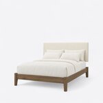 Diagonal angled view showing the left side of a modern upholstered bed, with a plain headboard, low rails and tapered legs.