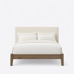 Front view of a modern upholstered bed, showing a wide rectangular headboard above a low foot rail on tapered square legs.