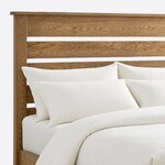 Headboard close-up of a minimalist slat bed, showing wide horizontal slats with open gaps below a thin overhanging cap rail.