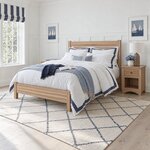 Diagonal angled room view showing the left side of a minimalist slat bed with a low footboard, in a white paneled bedroom.