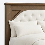 Headboard close-up of a transitional panel bed, showing a button-tufted arched insert framed by planked corners under a cap.