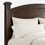 Headboard close-up of a traditional poster bed, showing the molded arched panel and a paneled post with a stepped cap.