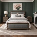 Front room view of an upholstered sleigh bed with leather inlay panels, in a green-paneled bedroom with a fireplace.