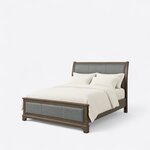 Diagonal angled view showing the left side of an upholstered sleigh bed, with leather inlay panels and a low footboard.