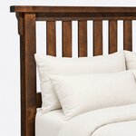 Headboard close-up of a rustic slat bed, showing the overhanging cap rail, a corbel bracket and flat vertical slats.