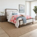 Diagonal angled room view showing the right side of a modern upholstered bed with a framed footboard, in a coastal bedroom.