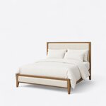 Diagonal angled view showing the left side of a modern upholstered bed, with a wood-framed headboard and a low footboard.