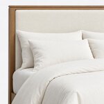 Headboard close-up of a modern upholstered bed, showing the upholstered panel set in a wood frame under a stepped cap rail.