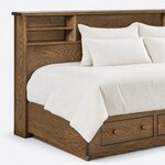 Headboard close-up of a bookcase storage bed, showing the overhanging top cap, a shelved open cubby and the end stile.