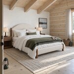 Diagonal angled room view showing the right side of a modern upholstered bed with square posts, in a beamed cabin bedroom.