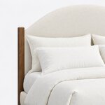 Headboard close-up of a modern upholstered bed, showing the arched headboard and a square post with a chamfered top.
