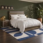 Diagonal angled room view showing the right side of a modern panel bed with metal bands, in an olive-green bedroom.