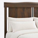 Headboard close-up of a contemporary panel bed, showing the wavy top rail, a square post and open gaps beside the panels.