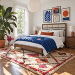 Diagonal angled room view showing the left side of a modern upholstered bed with a low footboard, in an eclectic bedroom.