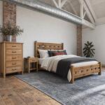 Diagonal angled room view showing the right side of a rustic bed with a slatted headboard, in a brick-walled loft bedroom.