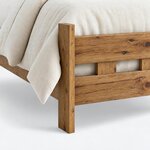 Footboard close-up of a rustic bed, showing a rectangular post continuing as a leg below the slatted footboard.