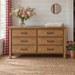 Front room view of a modern dresser with an overhanging slab top, in a cottage bedroom with gingham curtains.