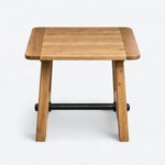 Front view of a rustic coffee table, with an overhanging top and a low metal stretcher between splayed legs.