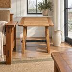 Front room view of a rustic coffee table with a plank top and a splayed base, in a paneled farmhouse living room.