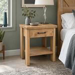 Diagonal angled room view showing the right side of a rustic nightstand with a metal bar pull, in a grey-green bedroom.