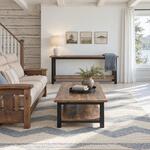 Front room view of a rustic console table with a low shelf, in a log-walled living room with ceiling beams.